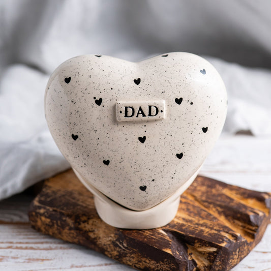 Hand-painted heart-shaped ceramic urn with a minimalist design of small black hearts on a matching stand.
