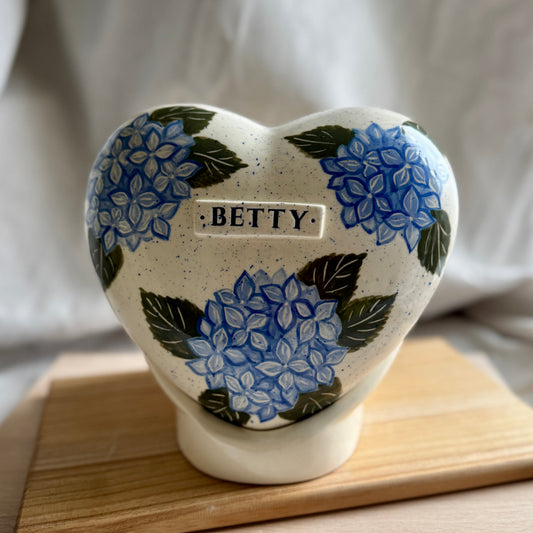 Hand-painted heart-shaped ceramic urn with a lush blue hydrangea bloom and matching stand for human or pet ashes.