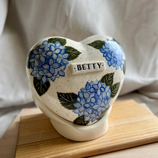Side profile of the blue hydrangea memorial urn on its stand, highlighting the smooth glaze and handmade pottery quality.