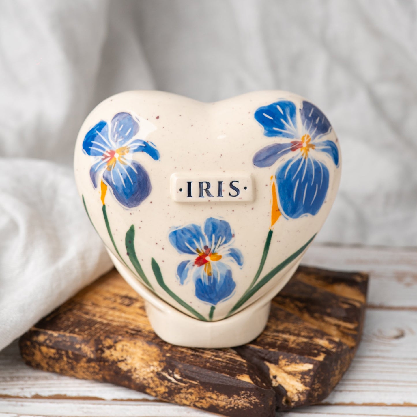 Hand-painted heart-shaped ceramic urn with blue irises and a matching stand for human or pet ashes.