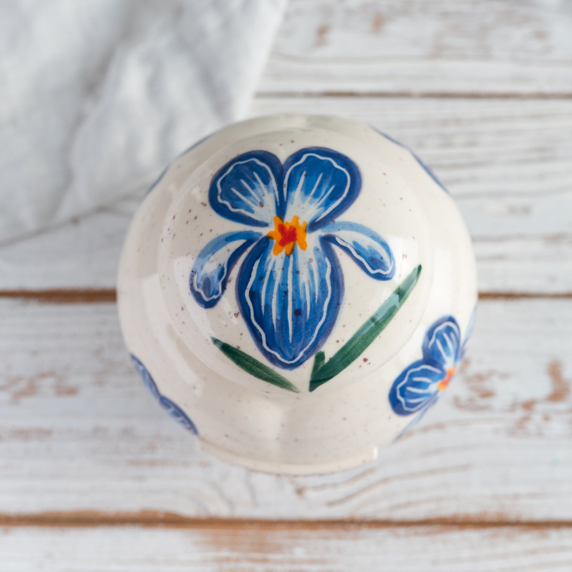 Top-down view of hand-painted ceramic lid with blue iris flower design for heart keepsake urn