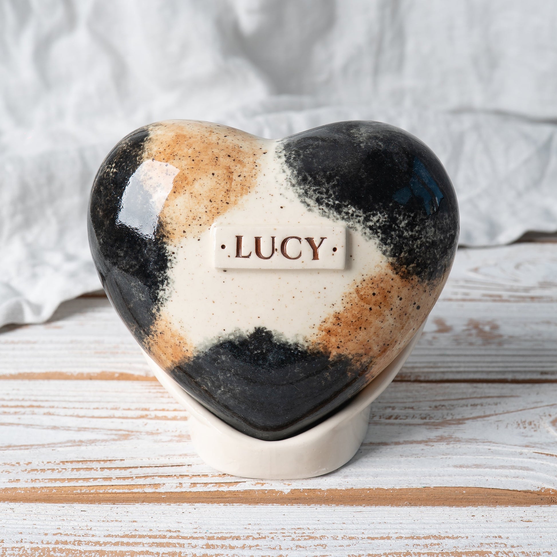 Hand-painted heart-shaped ceramic urn for a calico cat, featuring orange, black, and white patches with floral accents, includes a ceramic stand.