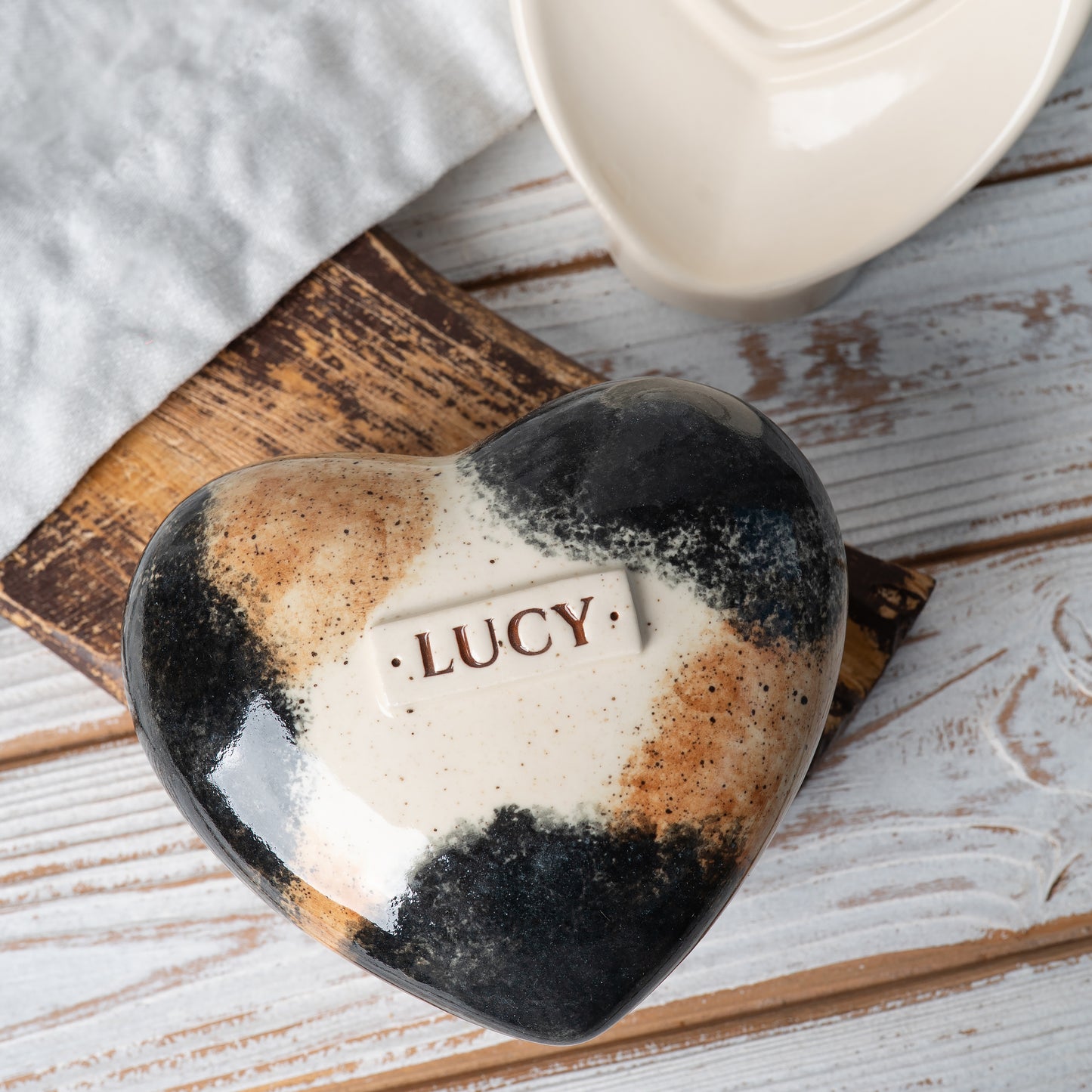 Top view of a heart-shaped calico cat urn, showing hand-painted orange, black, and white patches.