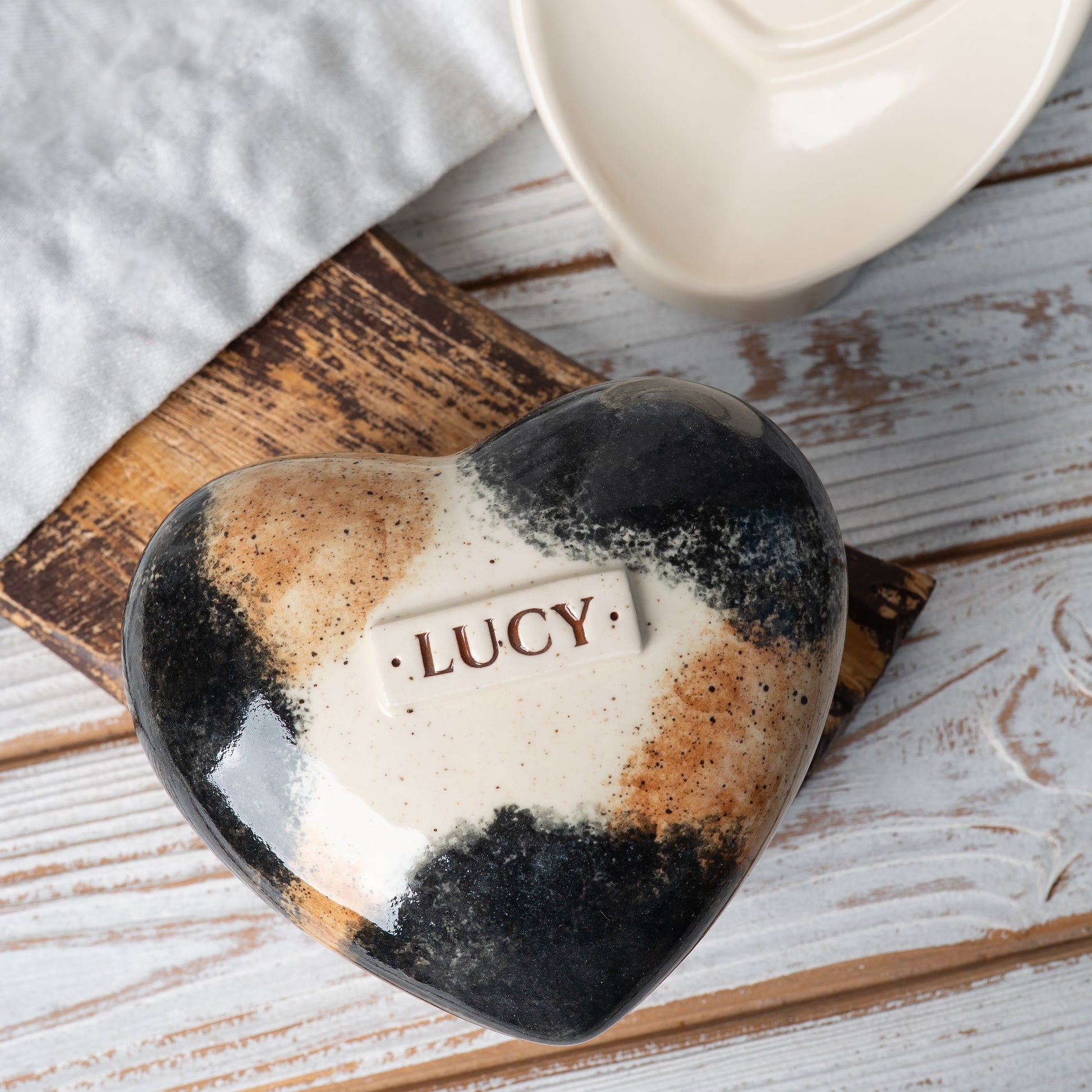 Top view of a heart-shaped calico cat urn, showing hand-painted orange, black, and white patches.