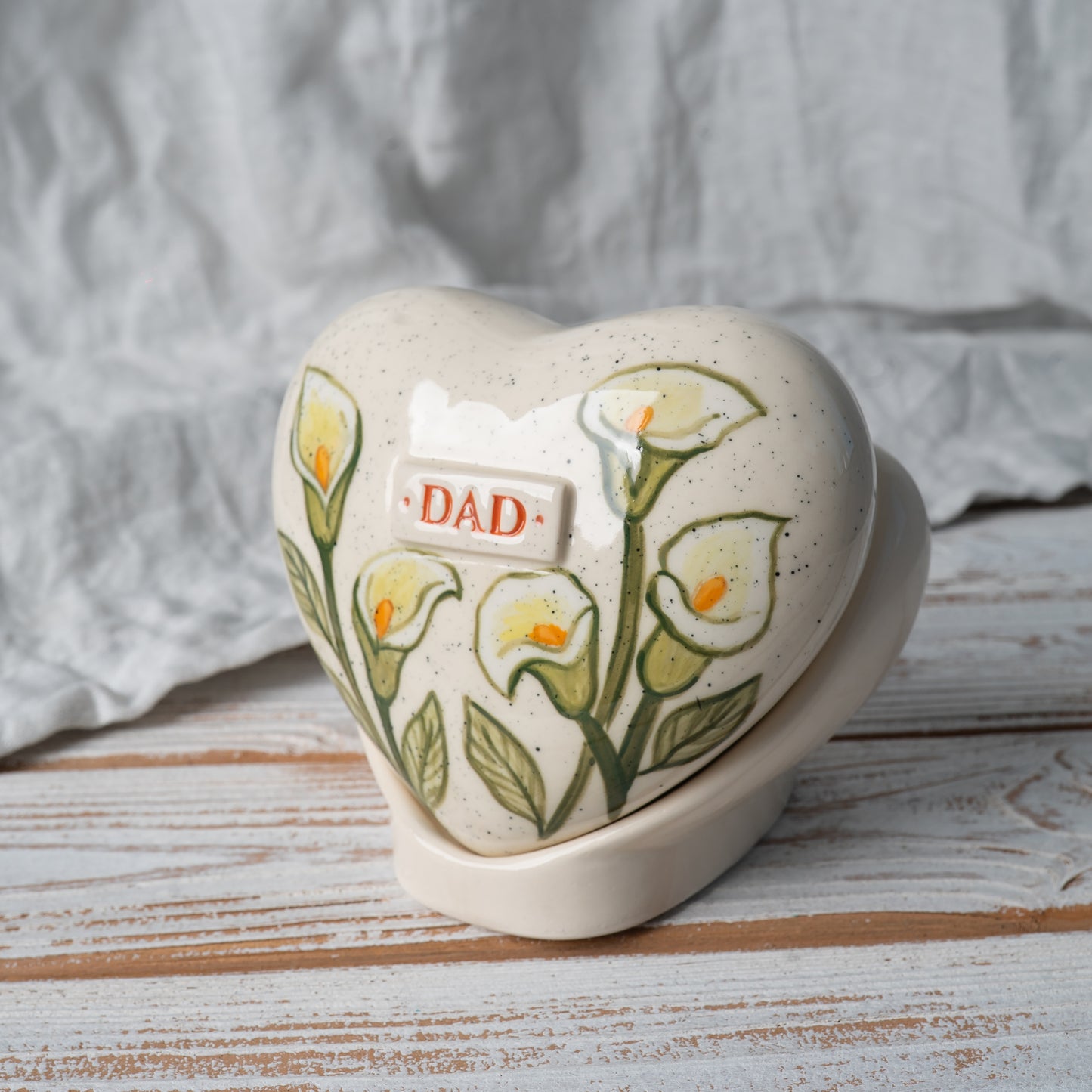 Side profile of the white lily ceramic heart urn on its stand, highlighting the slim, elegant shape and artisan pottery craftsmanship.