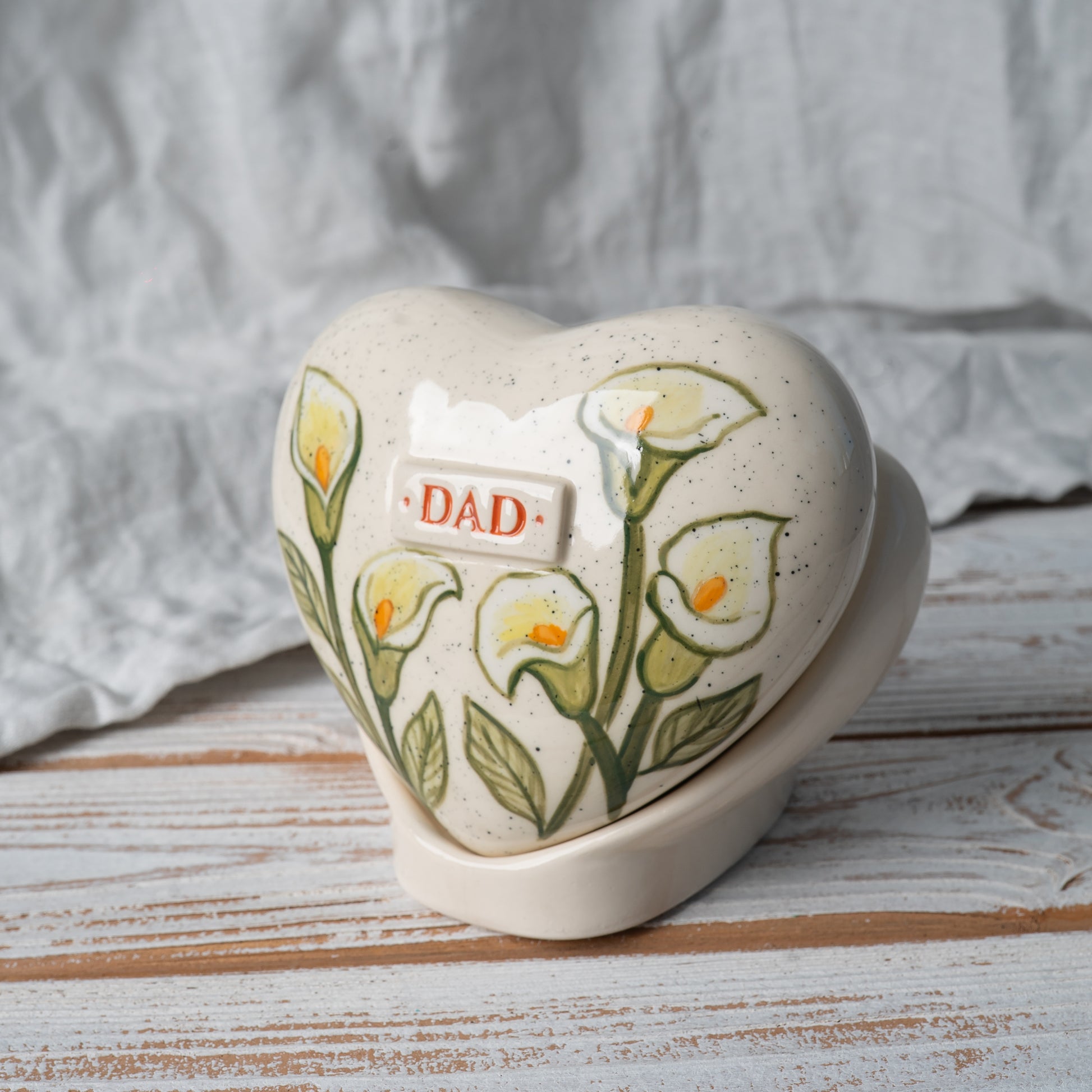 Side profile of the white lily ceramic heart urn on its stand, highlighting the slim, elegant shape and artisan pottery craftsmanship.