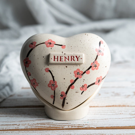 Hand-painted heart-shaped ceramic urn with soft pink cherry blossoms and a matching stand for human or pet ashes.