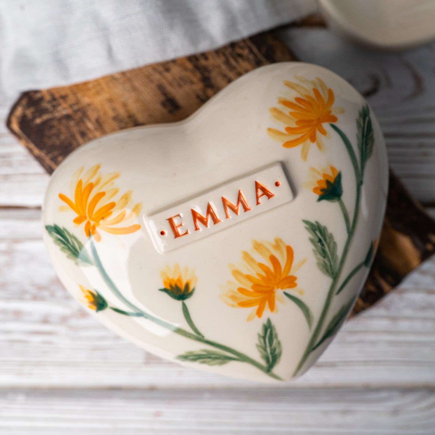 Top view of the ceramic heart urn, showing the detailed golden chrysanthemum petals and green leaf accents.