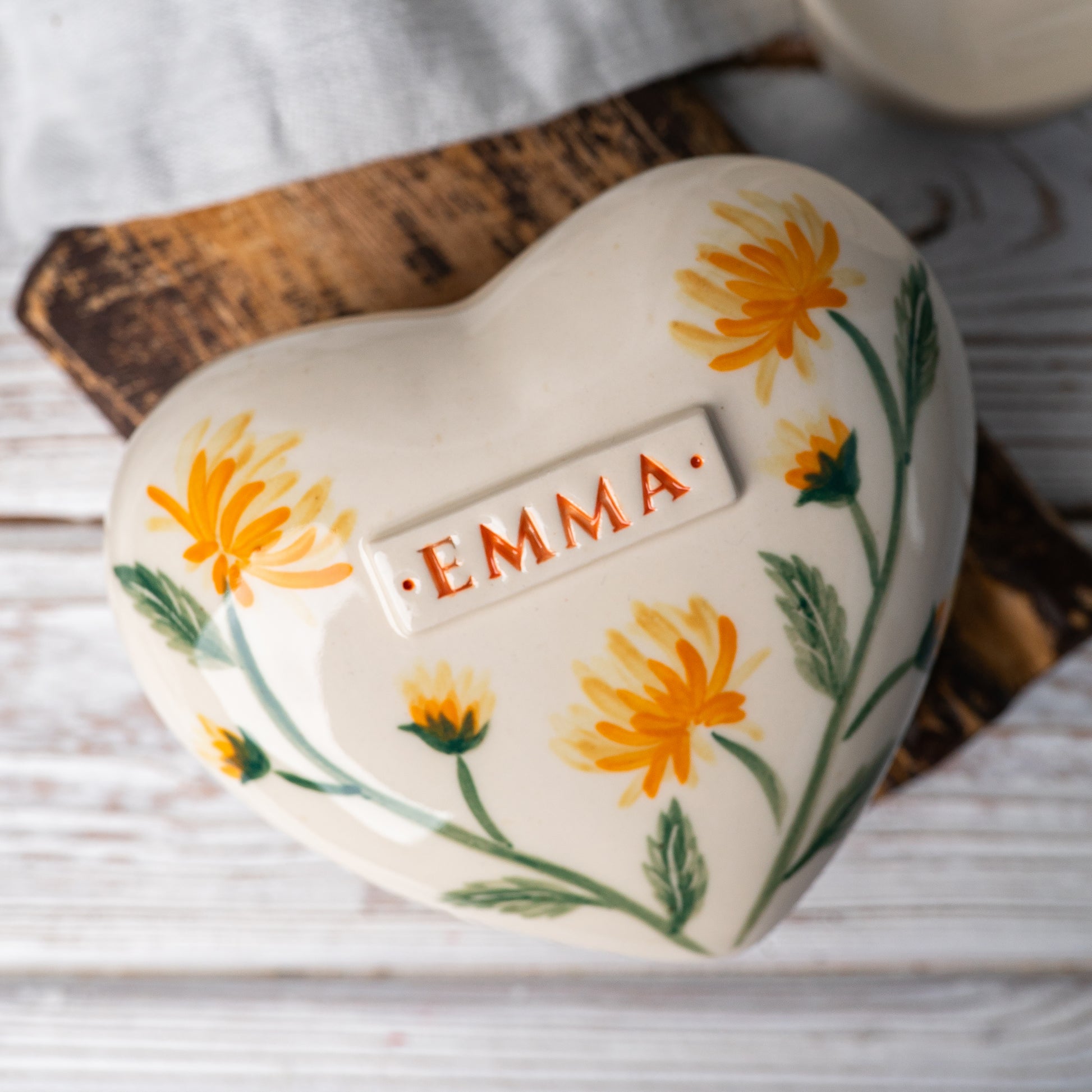 Top view of the ceramic heart urn, showing the detailed golden chrysanthemum petals and green leaf accents.