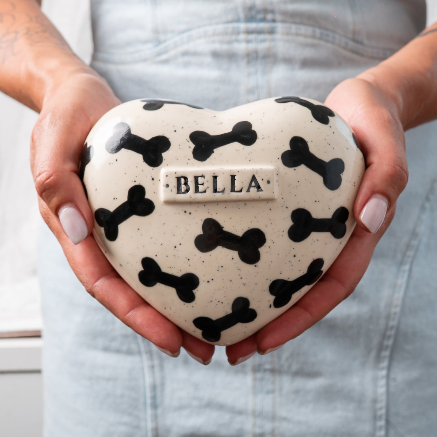 Small custom heart-shaped ceramic dog keepsake urn held gently in hands for scale