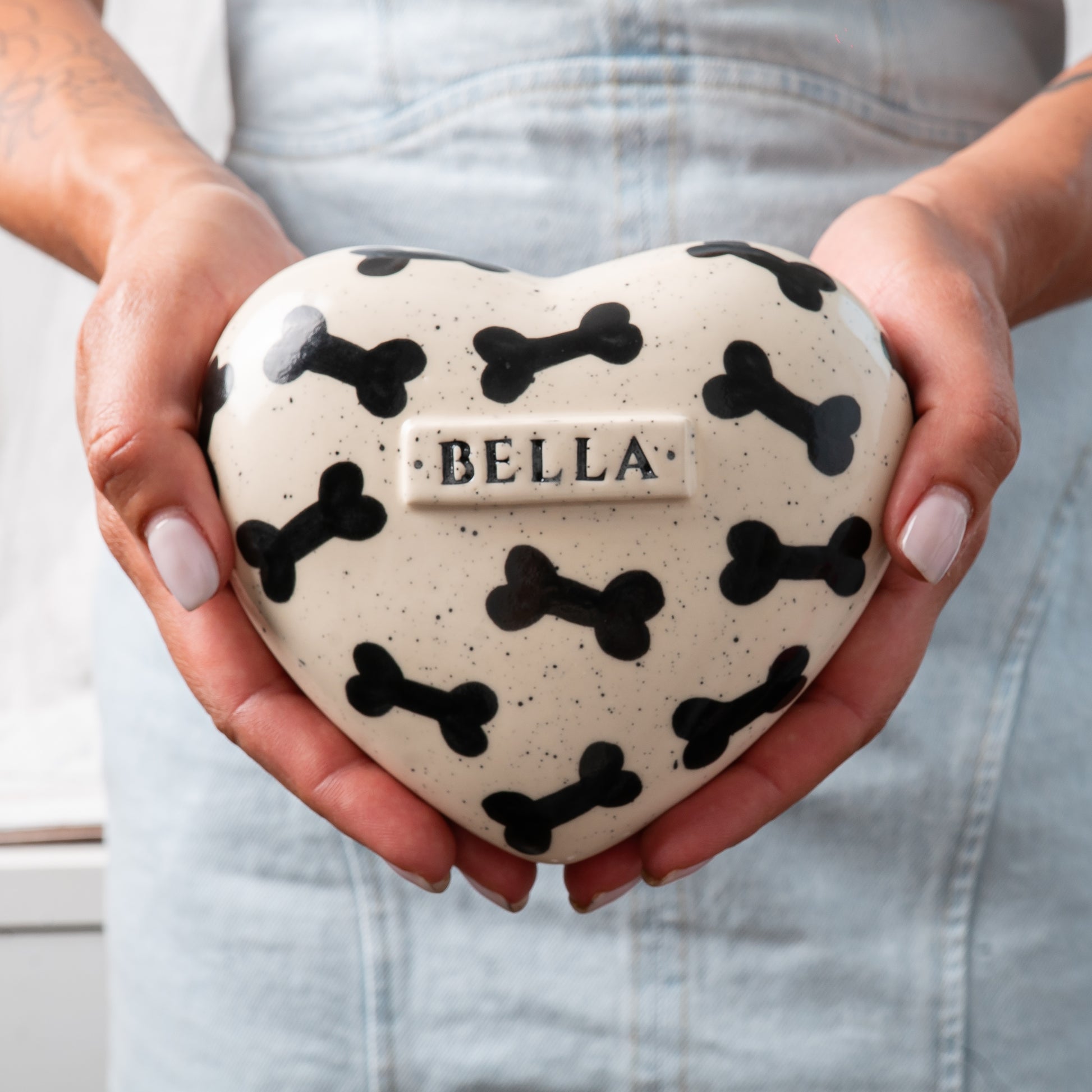 Small custom heart-shaped ceramic dog keepsake urn held gently in hands for scale