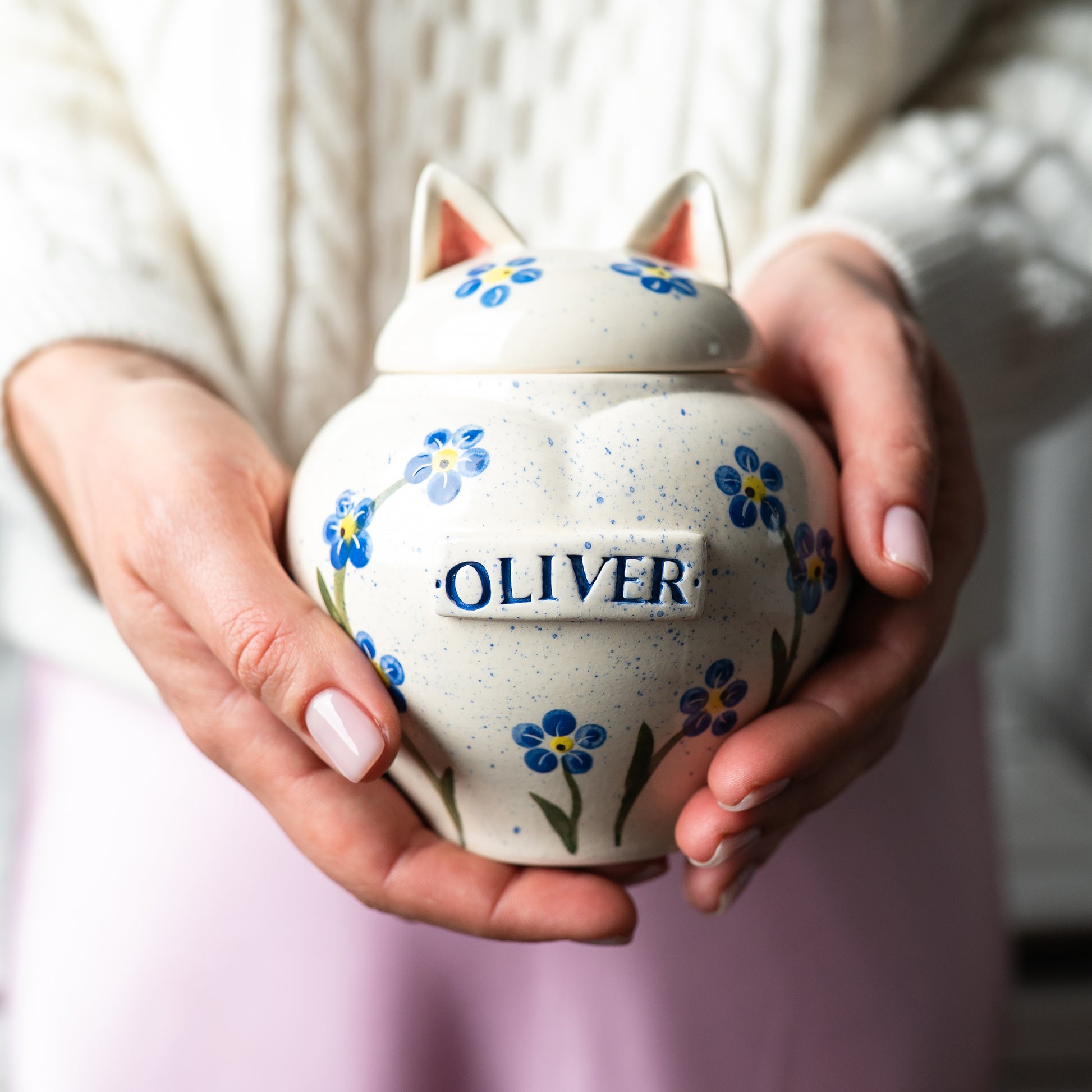 Close-up showing the size of the forget-me-not heart-shaped ceramic cat keepsake urn with ears held gently in hands.