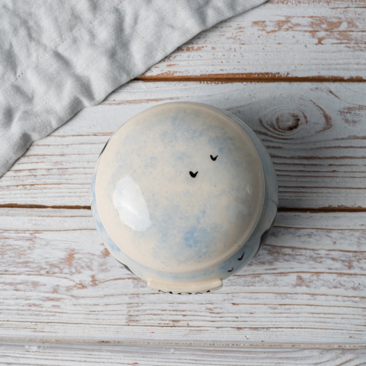 Top-down view of ceramic urn lid showing soft hand-painted sky motif