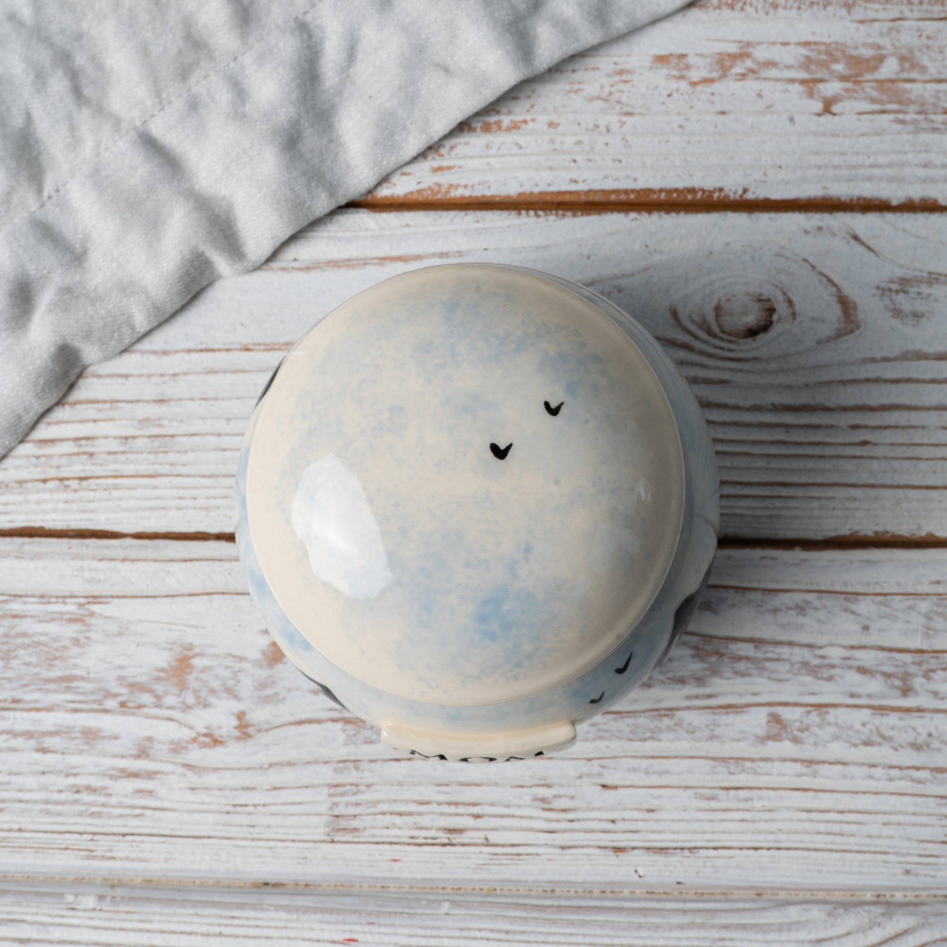Top-down view of ceramic urn lid showing soft hand-painted sky motif