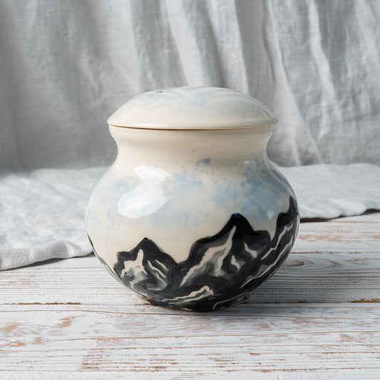 Side view of hand-painted ceramic urn featuring majestic snowy mountain peaks and soft sky