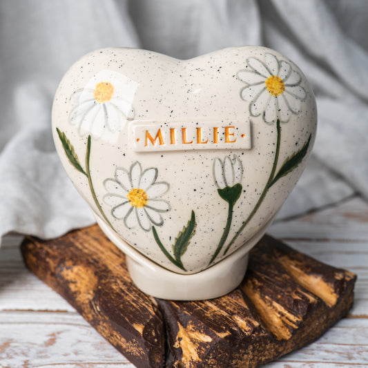 Hand-painted heart-shaped ceramic urn with white daisies and a matching stand for human or pet ashes.