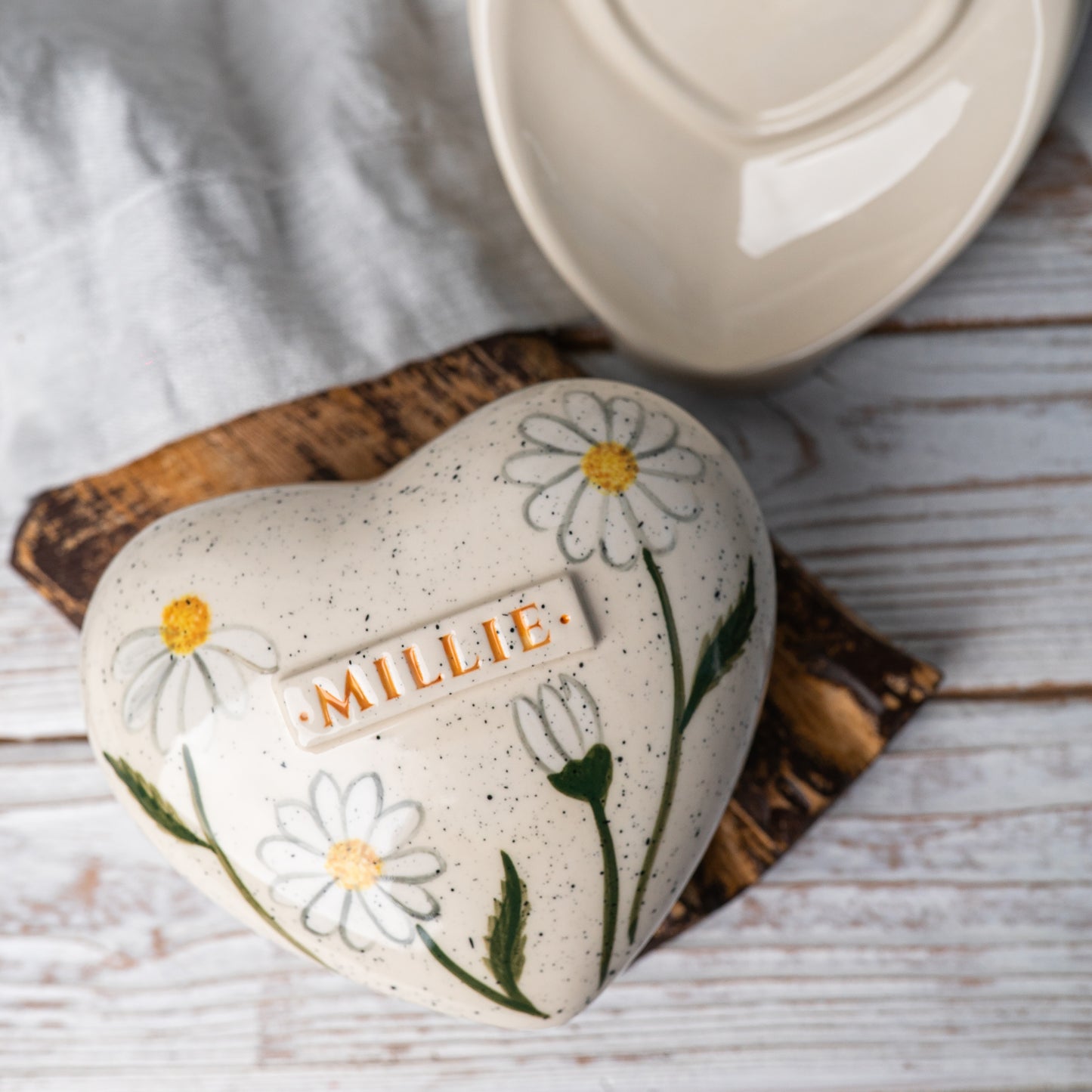 Top view of the ceramic heart urn, showing the detailed white daisy petals and sunny yellow centers.