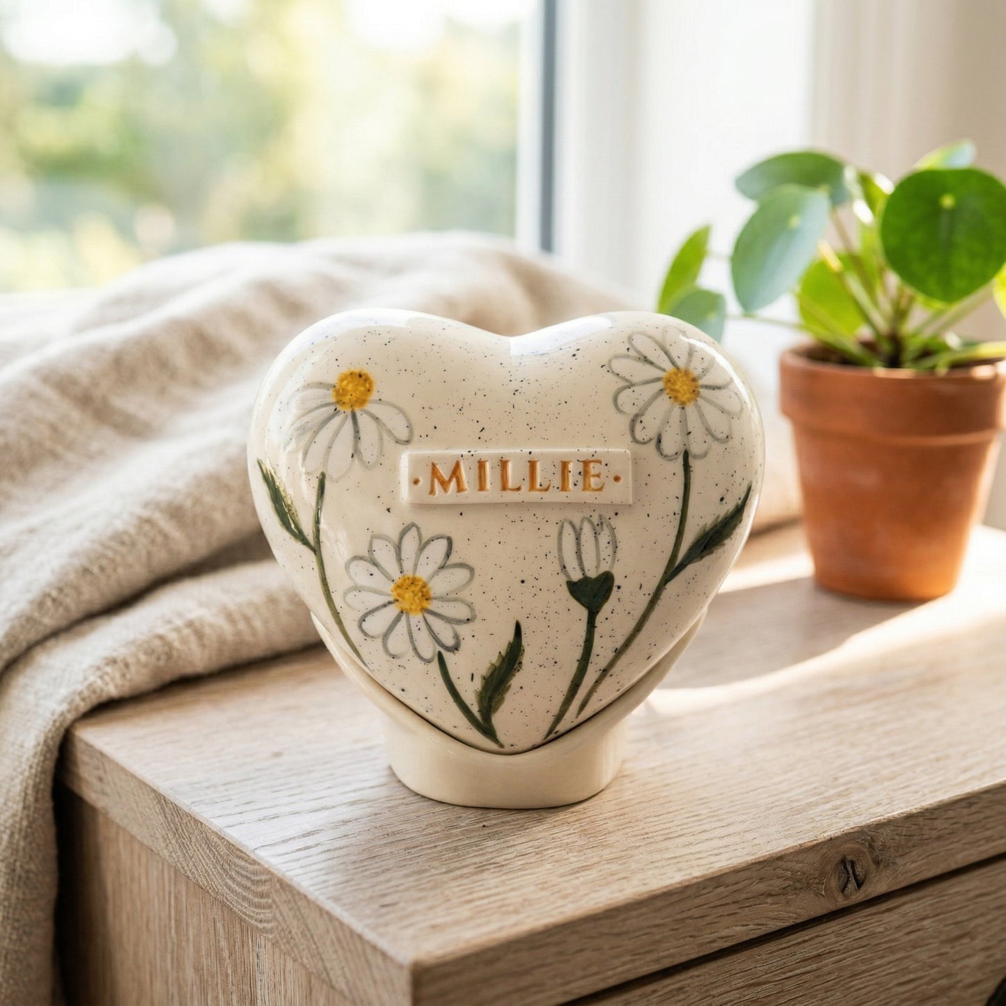 A bright home memorial display with a daisy flower heart urn on a shelf.