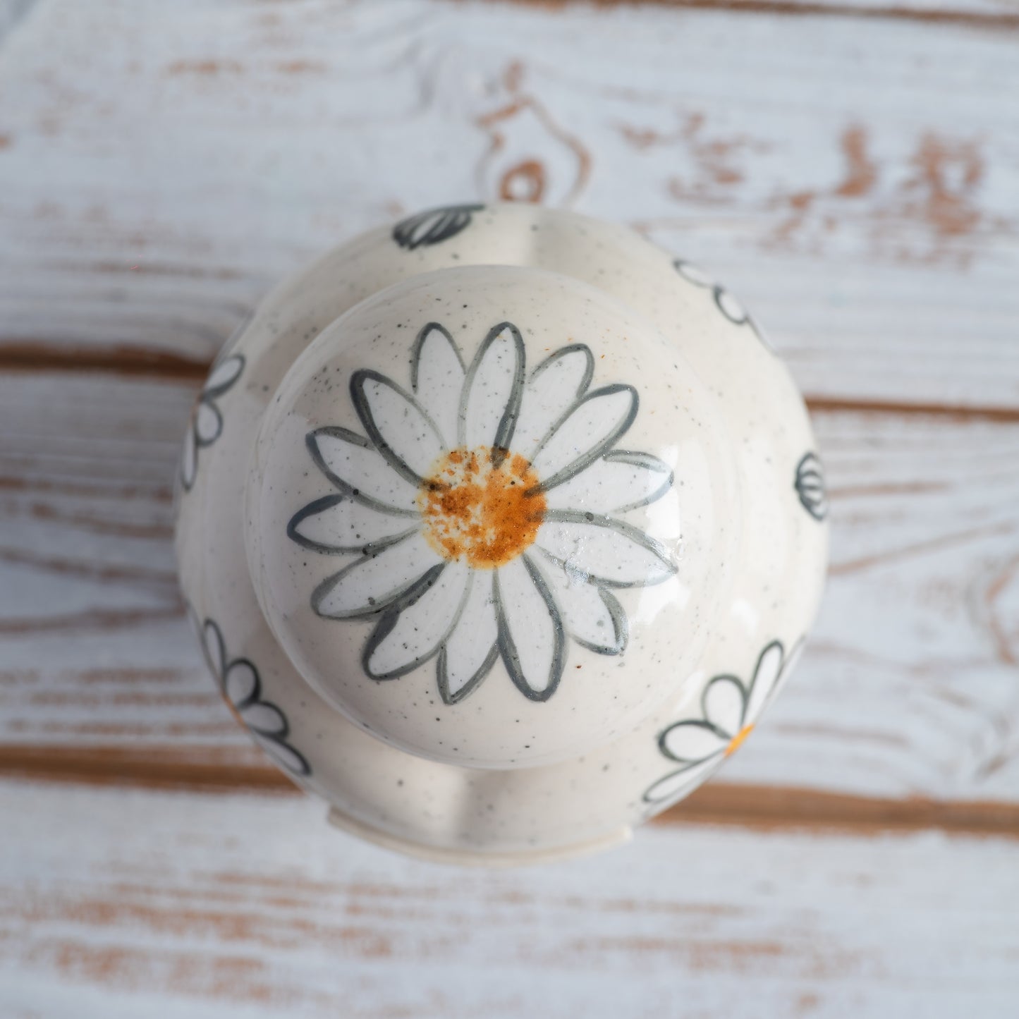 Close-up of the ceramic lid and hand-painted daisies on a white heart-shaped urn.