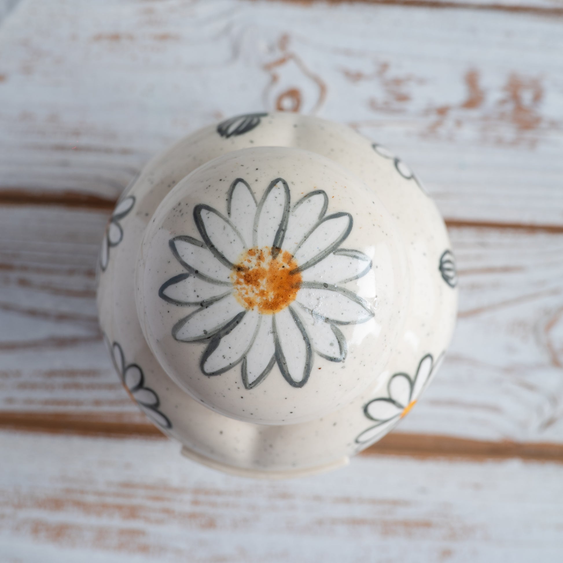 Close-up of the ceramic lid and hand-painted daisies on a white heart-shaped urn.