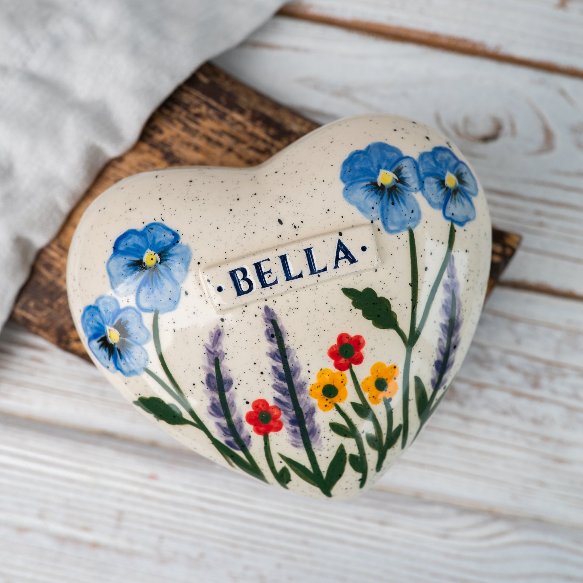 Top view of the ceramic heart urn showing the detailed hand-painted pansies, lavender, and red-yellow blossoms.
