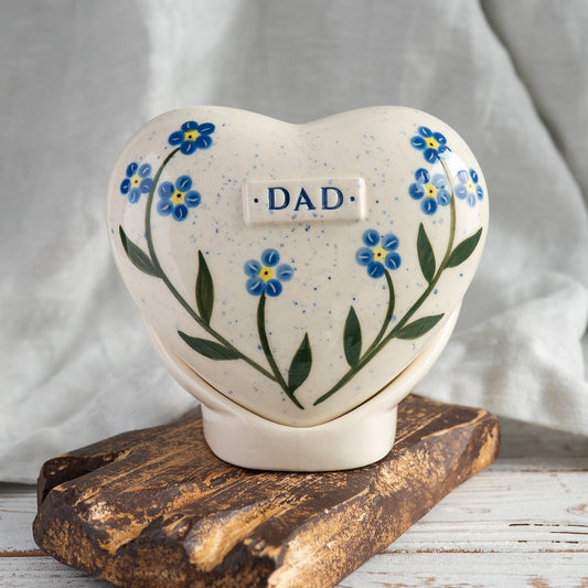 Hand-painted heart-shaped ceramic urn with blue forget-me-not flowers and a matching stand for human or pet ashes.