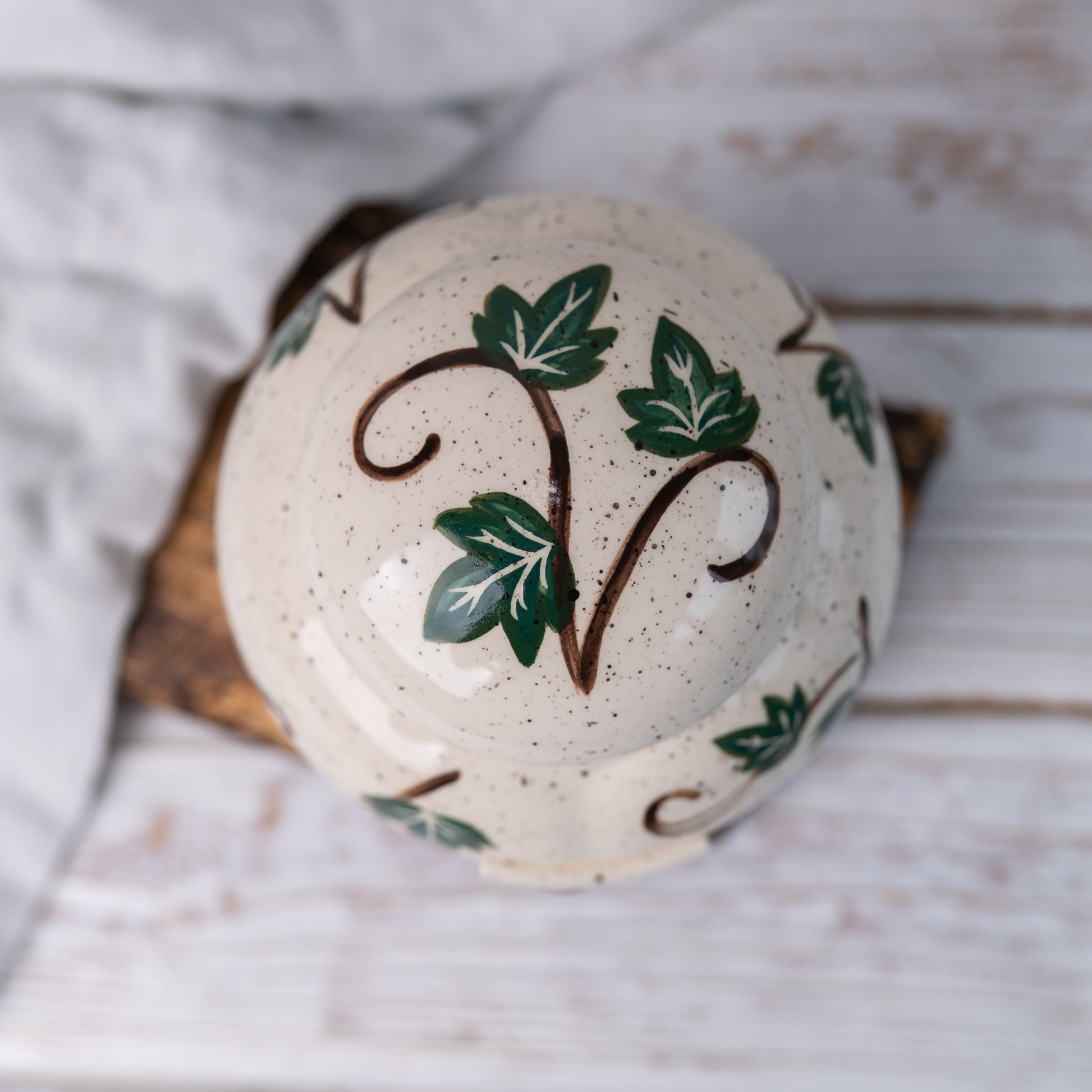 Top-down view of hand-painted ceramic lid with green ivy vine pattern for pet memorial urn