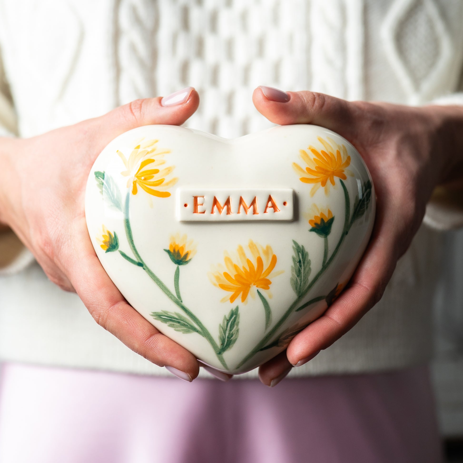 Holding a heart-shaped yellow chrysanthemum keepsake urn in hands to demonstrate the scale and hand-painted details.