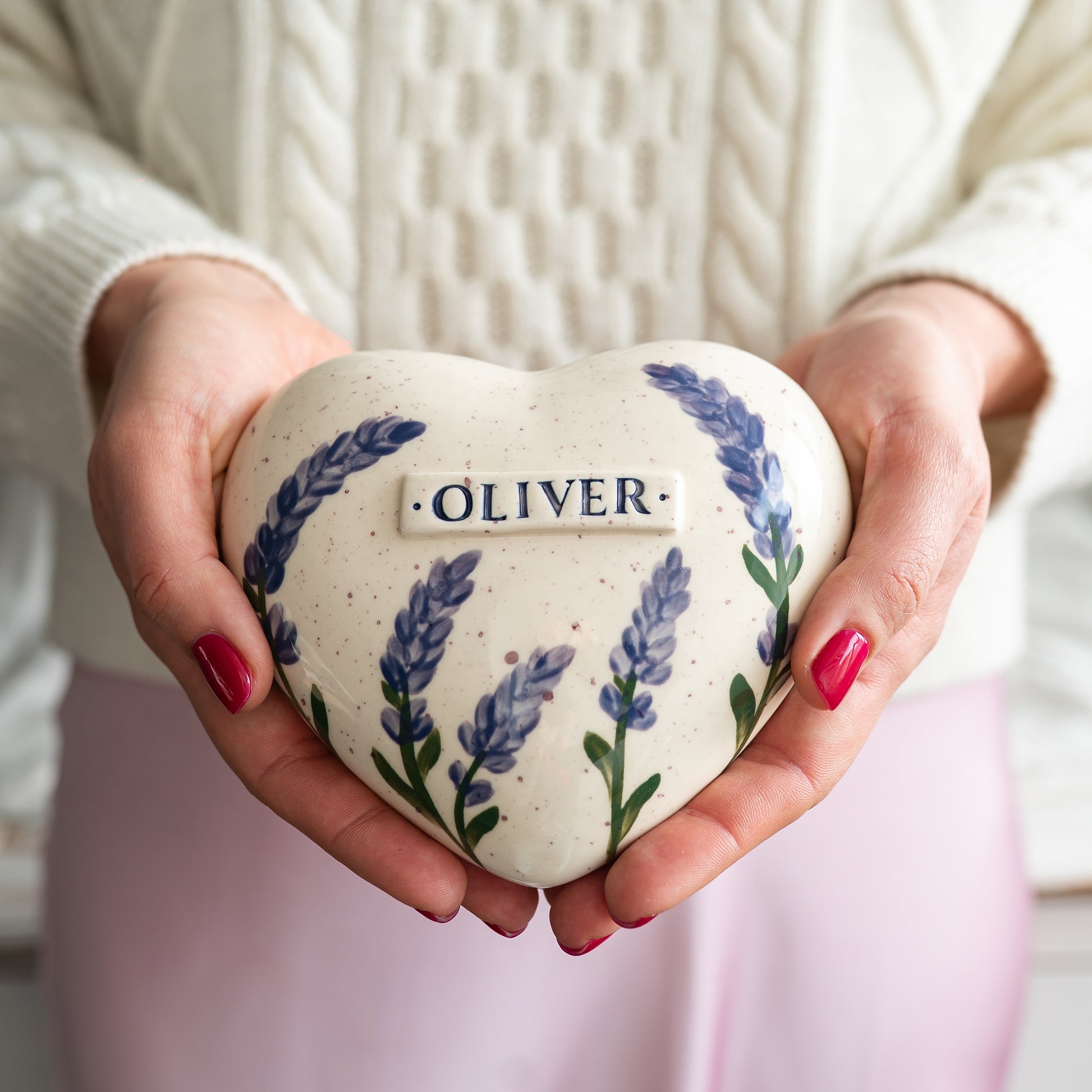 Holding a heart-shaped lavender small size keepsake urn in hands to demonstrate the scale and hand-painted details.