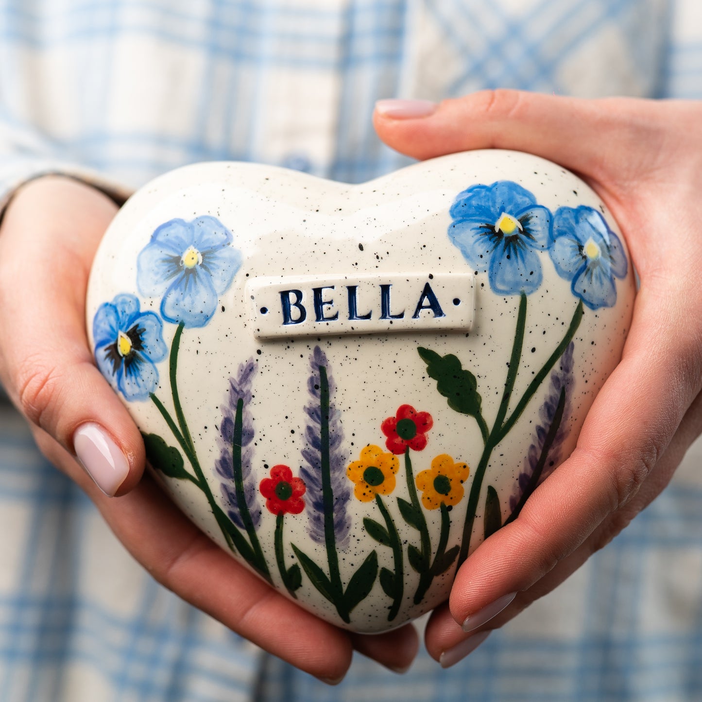 Holding a heart-shaped urn with a multi-flower design to show the artistic scale and hand-painted details.