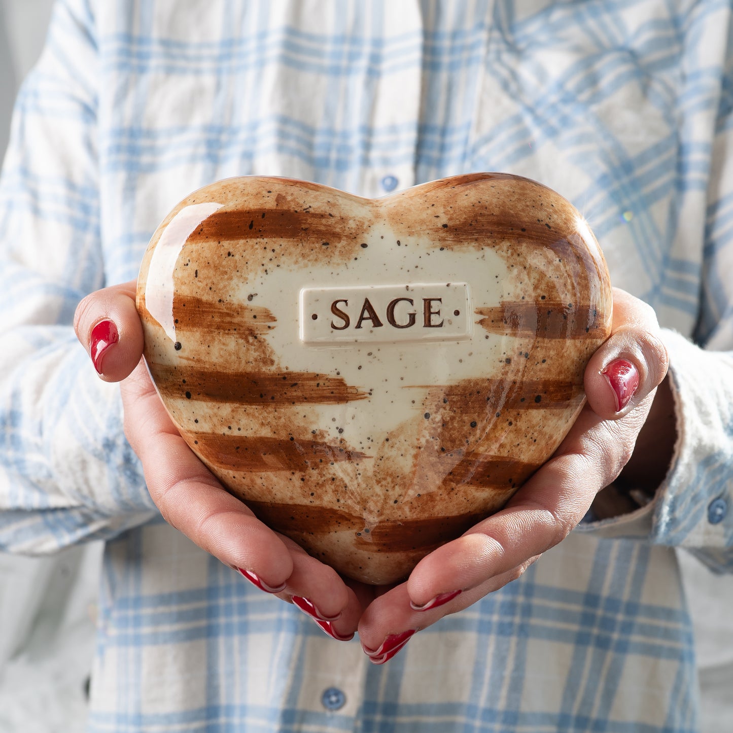 Holding a small, heart-shaped ceramic keepsake urn for an orange tabby cat in hands to show its scale and delicate hand-painted stripe pattern by Mira Ceramics.
