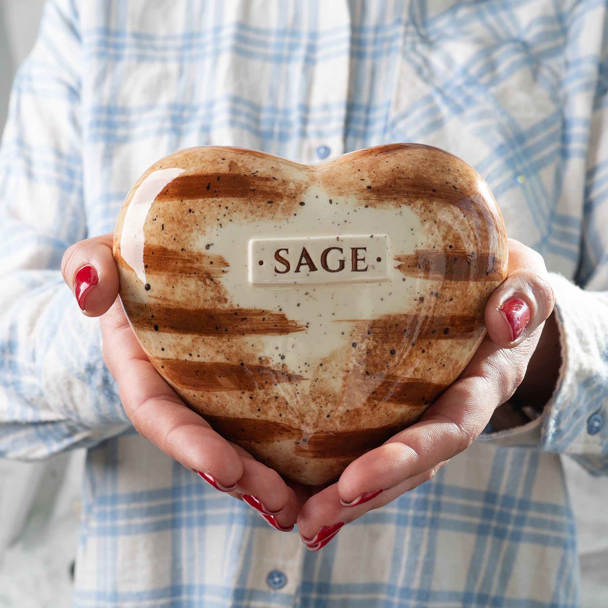 Holding a small, heart-shaped ceramic keepsake urn for an orange tabby cat in hands to show its scale and delicate hand-painted stripe pattern by Mira Ceramics.