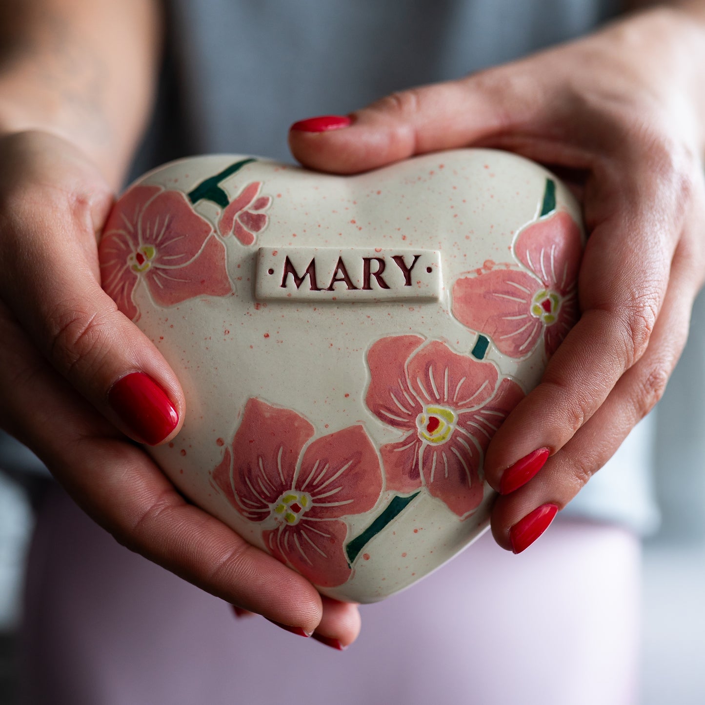Holding a heart-shaped orchid small size keepsake urn in hands to demonstrate the scale and hand-painted floral details.