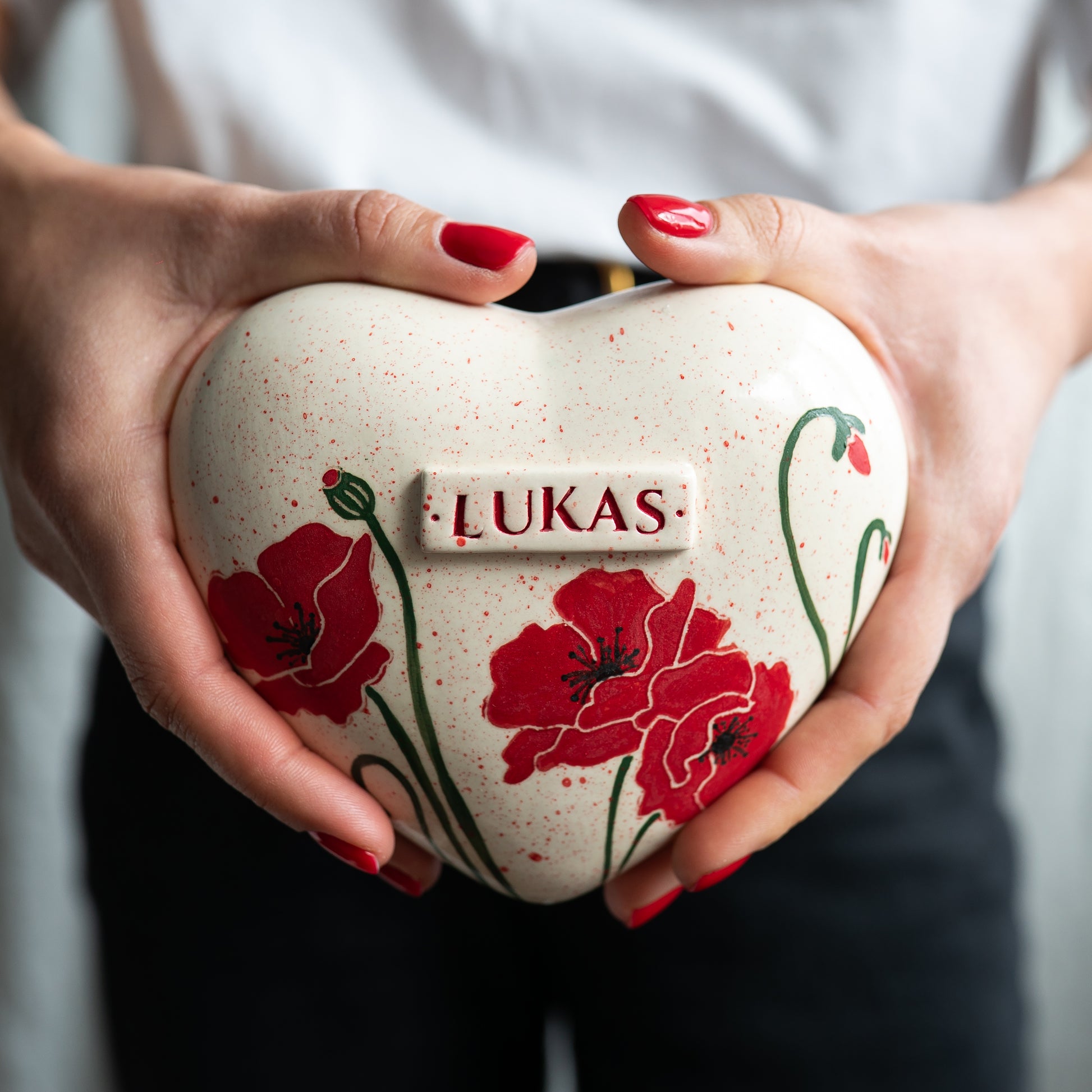 Holding a heart-shaped red poppy keepsake urn in hands to demonstrate the scale and hand-painted details.