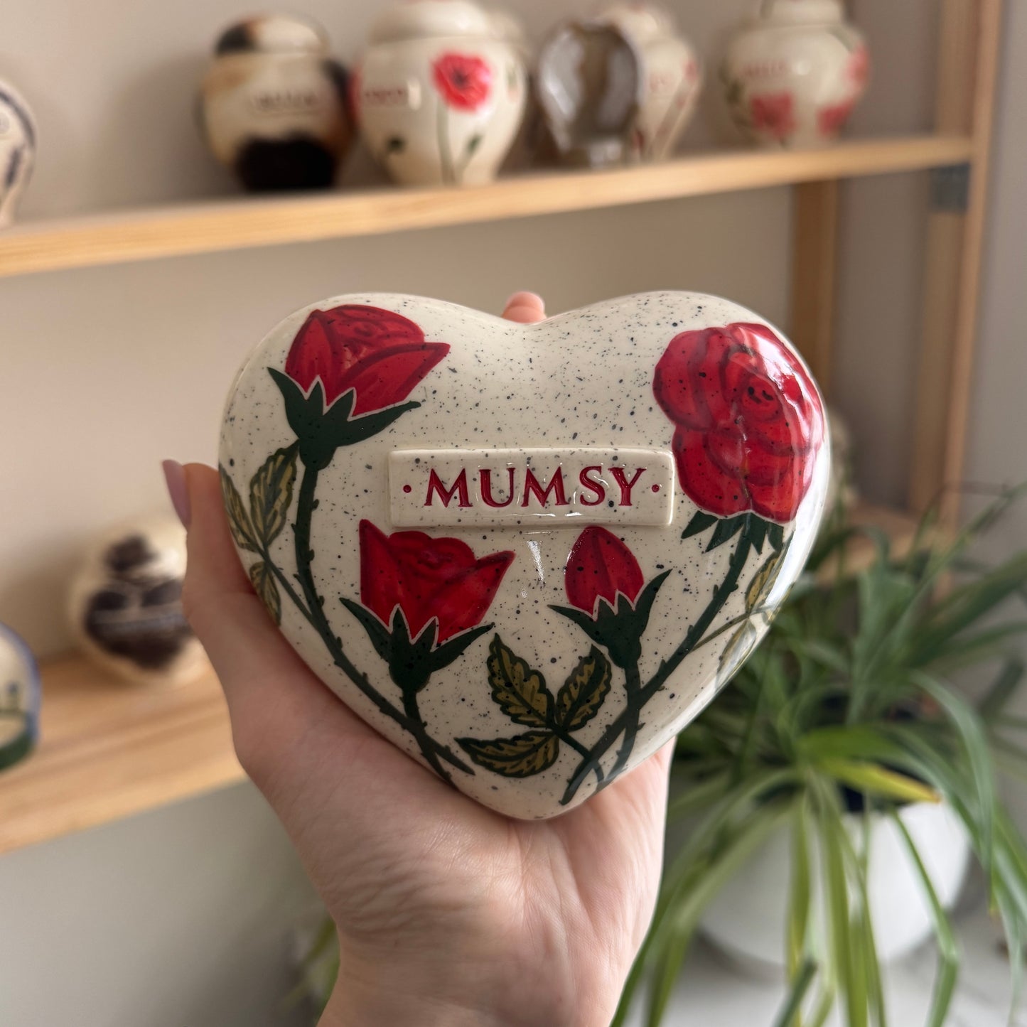 Holding a heart-shaped red rose keepsake urn in hands to demonstrate the scale and hand-painted details.
