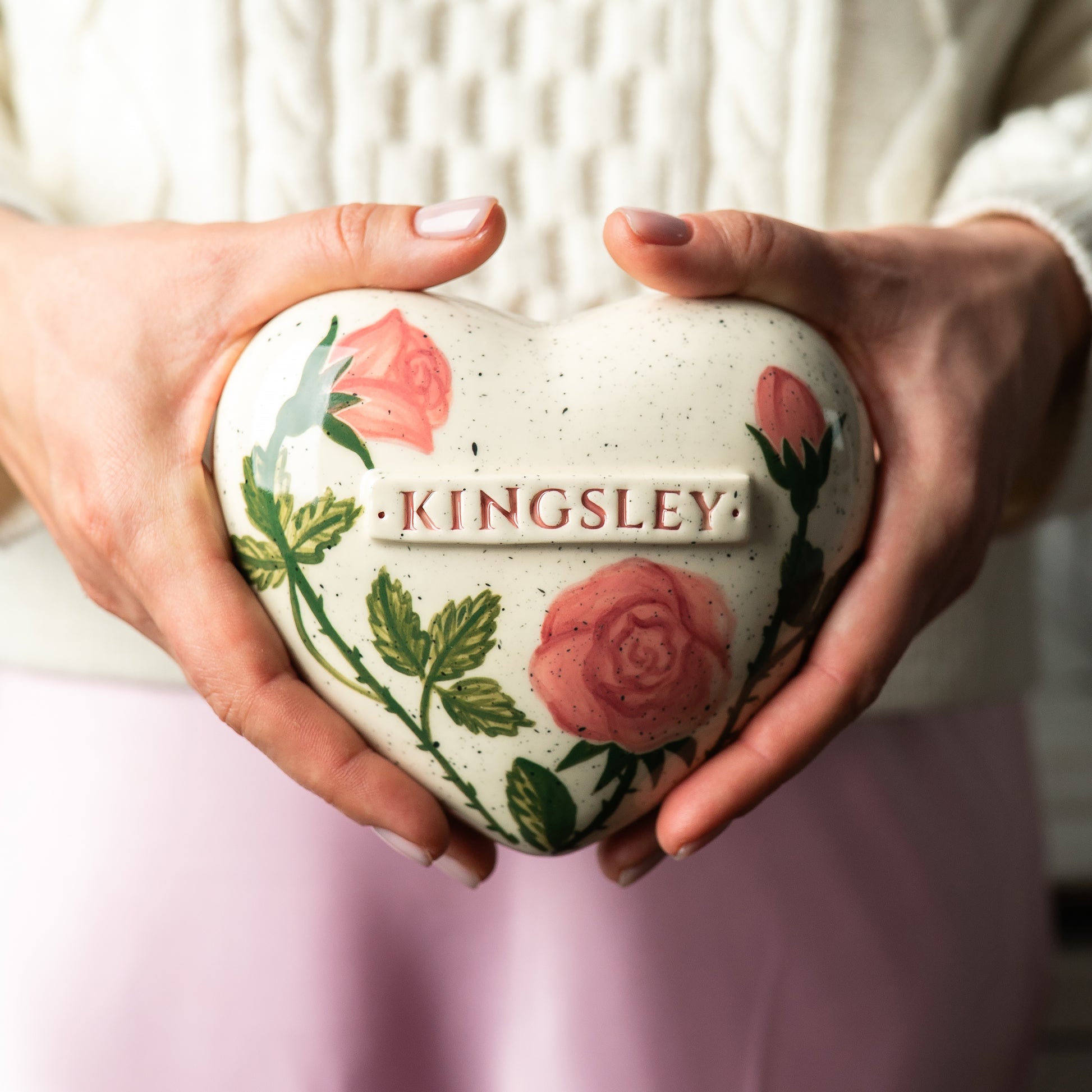 Holding a heart-shaped rose keepsake urn in hands to demonstrate the scale and hand-painted details.
