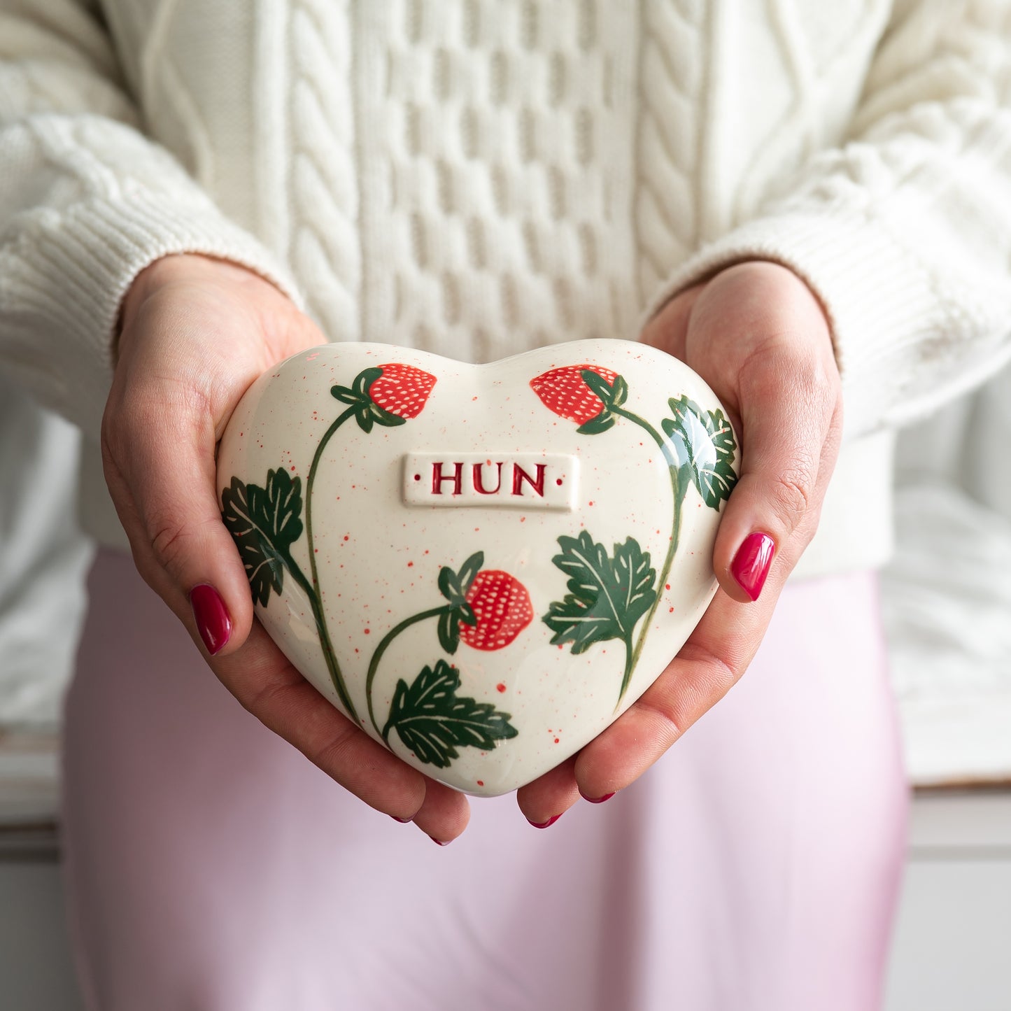 Holding a heart-shaped strawberry keepsake urn in hands to demonstrate the scale and hand-painted details.
