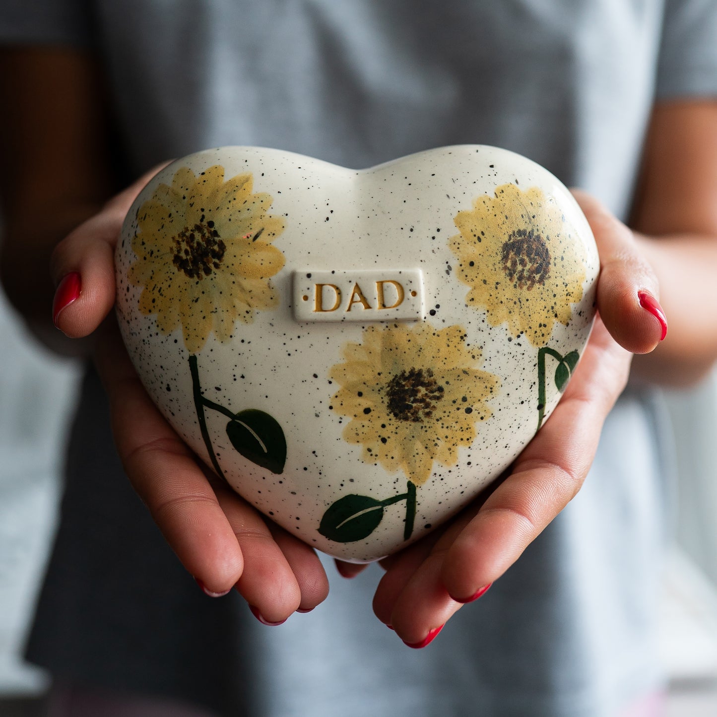 Holding a heart-shaped sunflower keepsake urn in hands to demonstrate the scale and hand-painted details.