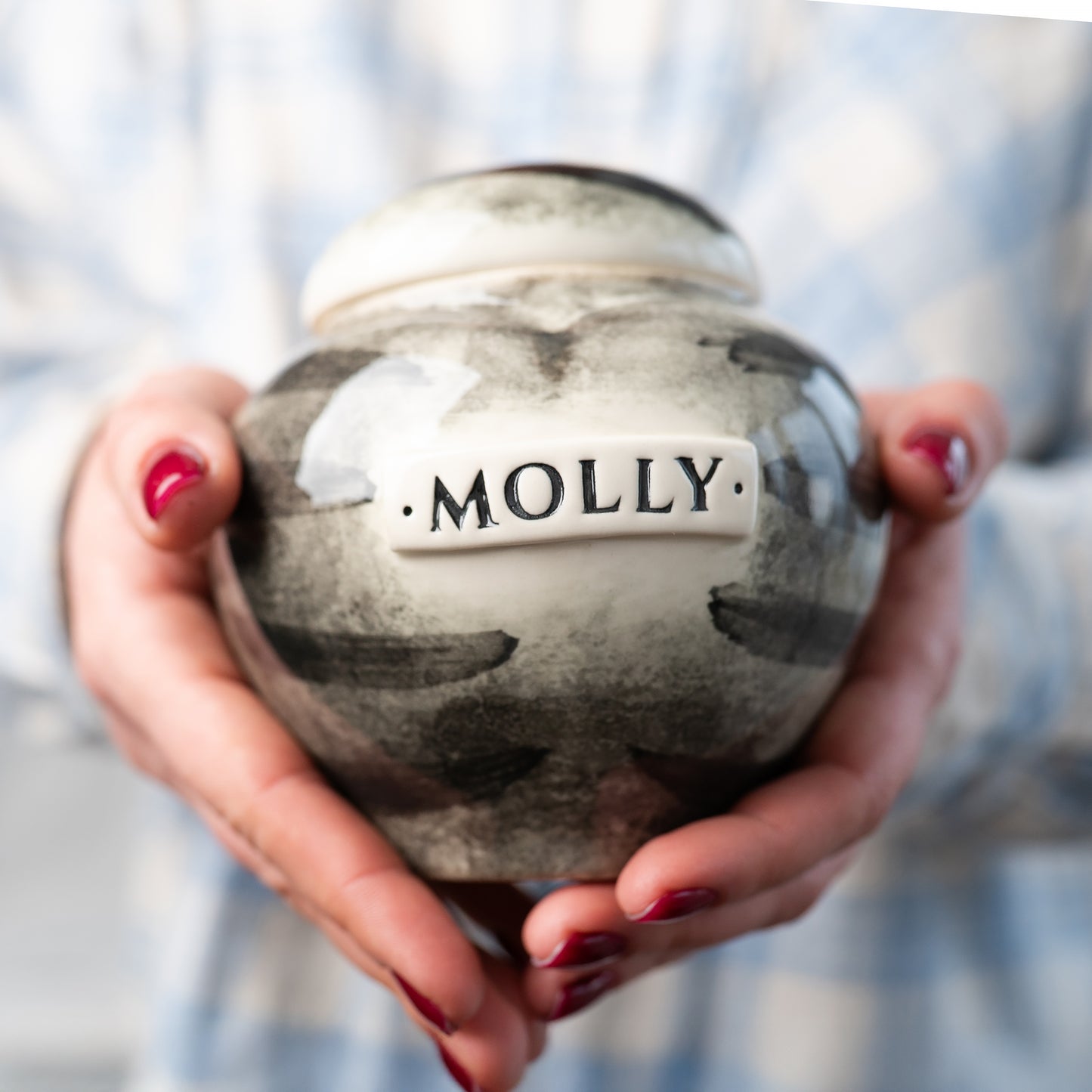 A person gently holds the grey tabby stripes cat keepsake heart urn to show its scale and artisan finish.