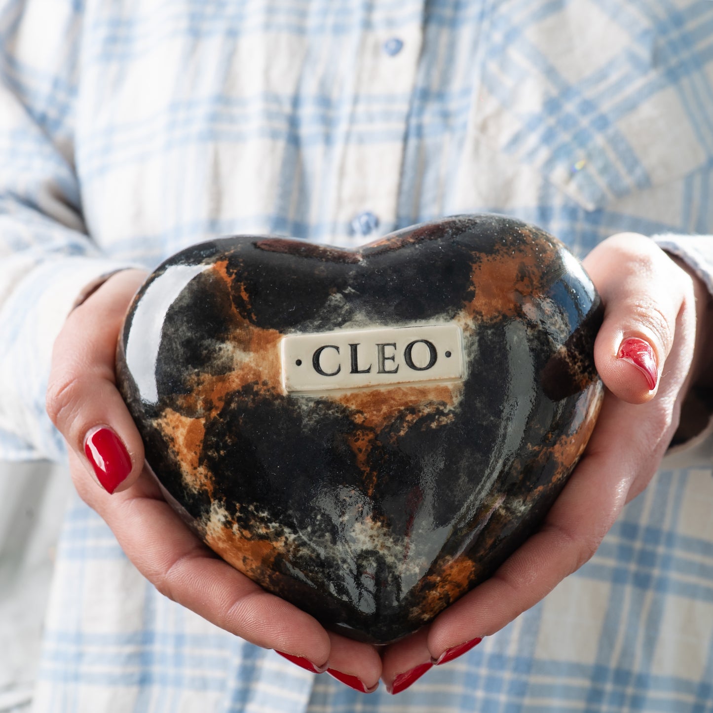 Holding a small handmade tortoiseshell cat heart-shaped keepsake urn in hands to show its scale and delicate craftsmanship.