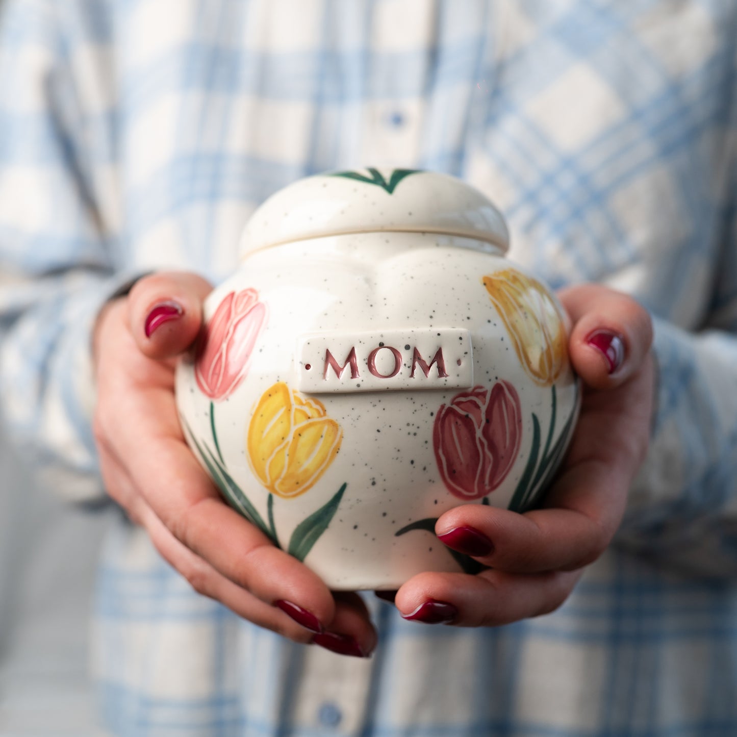 Close-up showing the small size of the tulip-patterned heart-shaped keepsake urn for Mom or Dad, held gently in hands for scale.