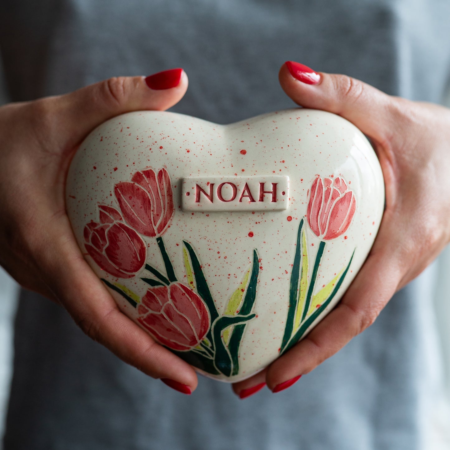 Holding a heart-shaped tulip keepsake urn in hands to demonstrate the scale and hand-painted details.