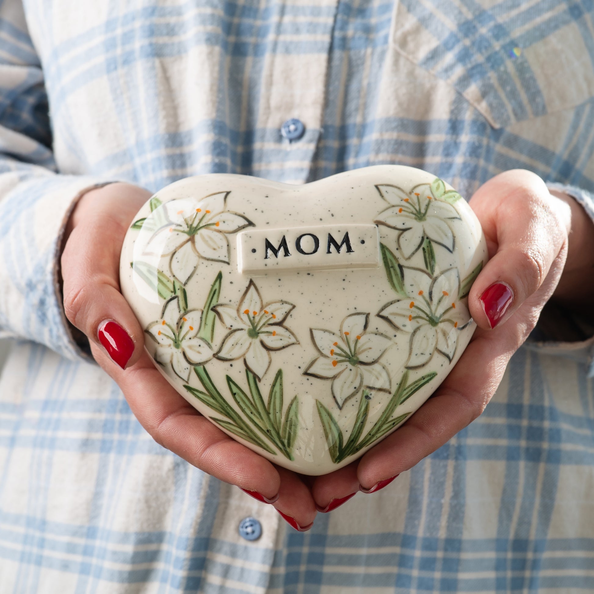 Holding a heart-shaped white lily keepsake urn in hands to demonstrate the scale and artisan detail.
