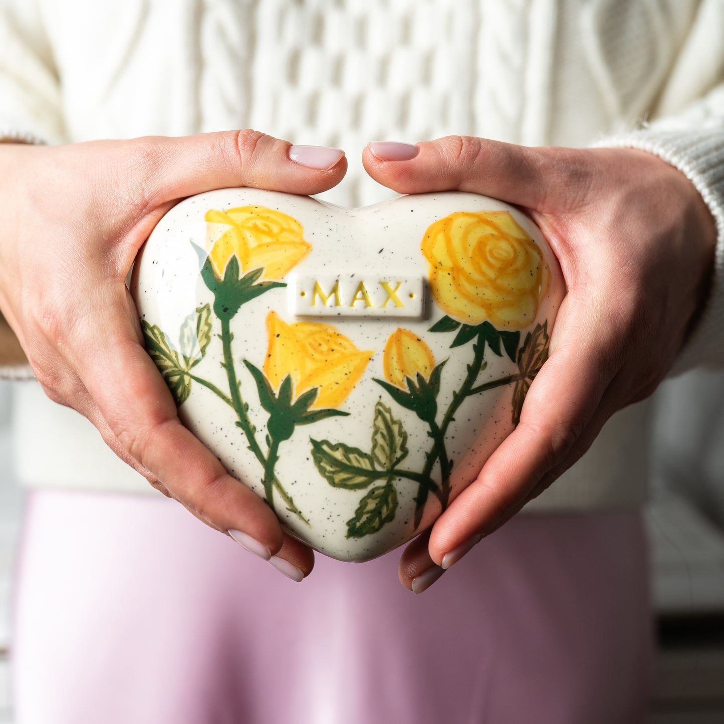 Holding a heart-shaped yellow rose small size keepsake urn in hands to demonstrate the scale and hand-painted details.