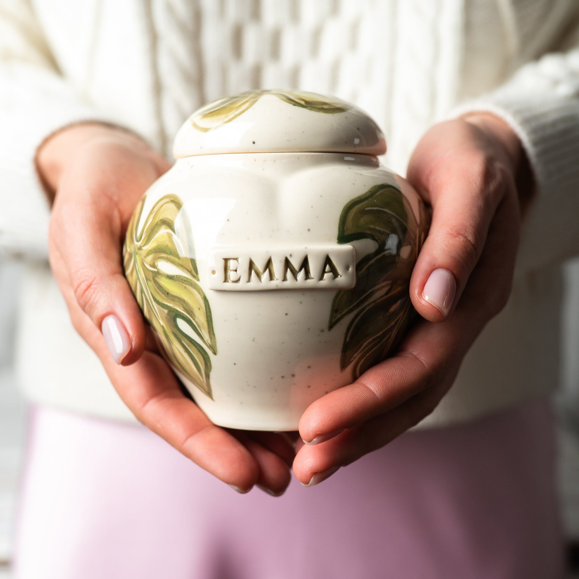 A person gently holding the monstera-themed cremation urn in their hands, demonstrating its realistic size, scale, and tactile finish.