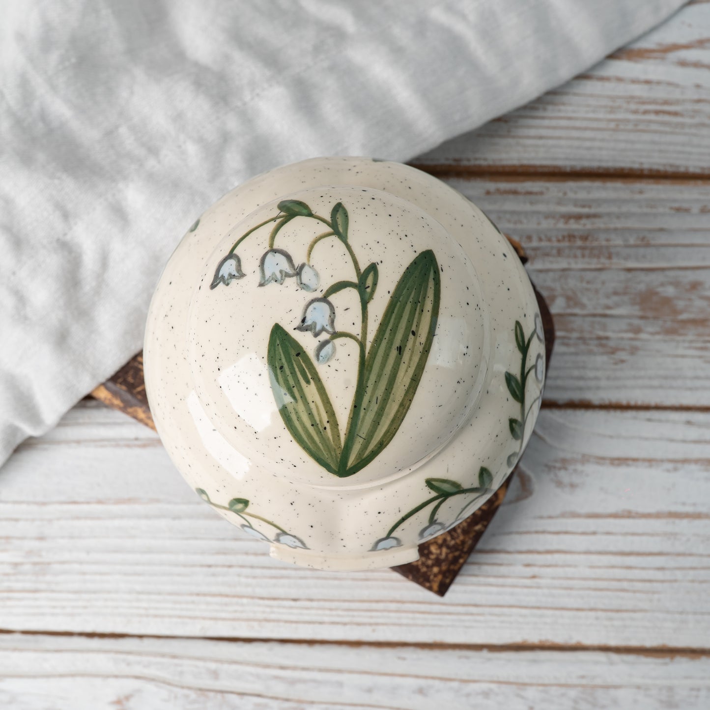Top-down view of hand-painted ceramic lid with lily of the valley design for heart keepsake urn