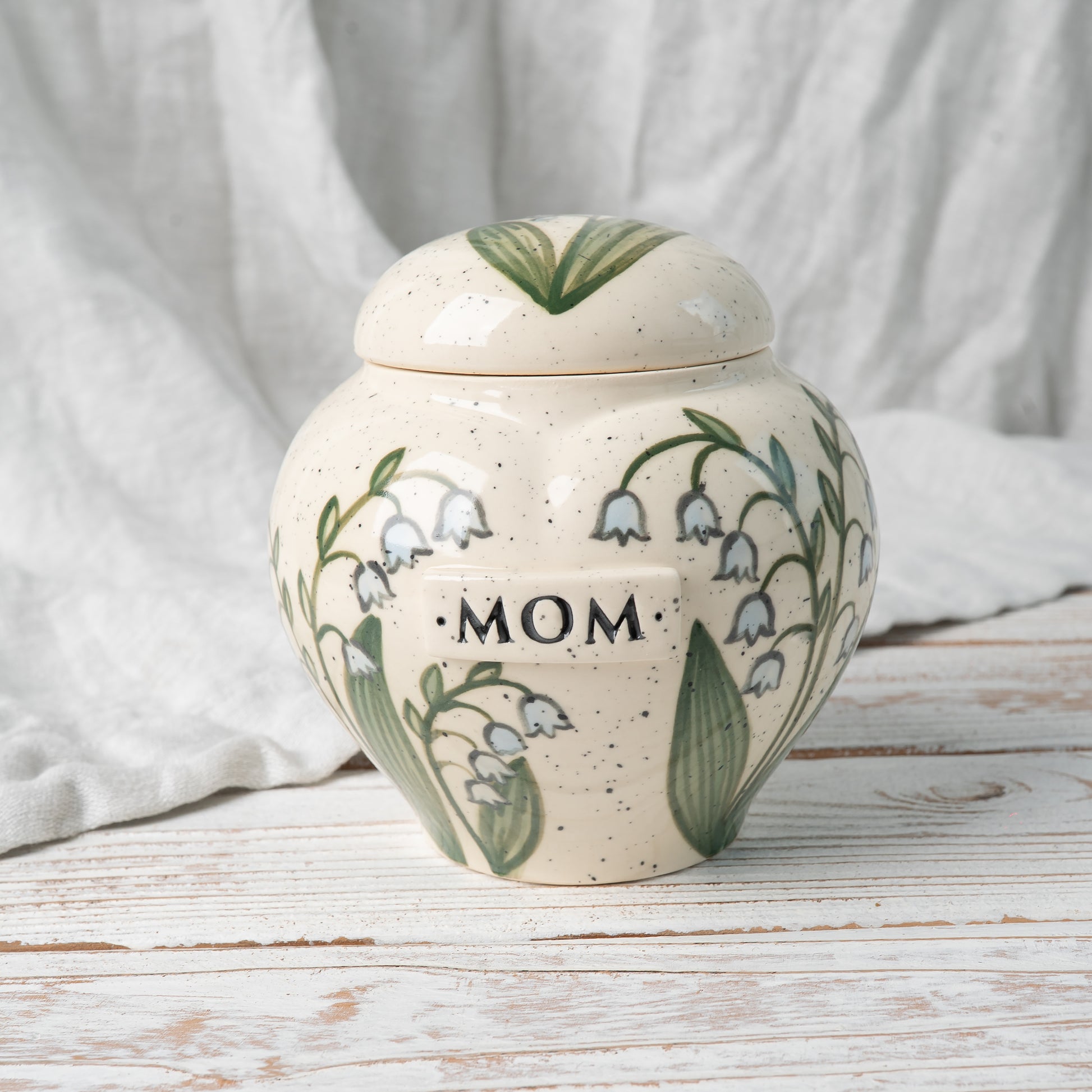 Side view of hand-painted heart ceramic memorial urn showing lily of the valley floral artwork
