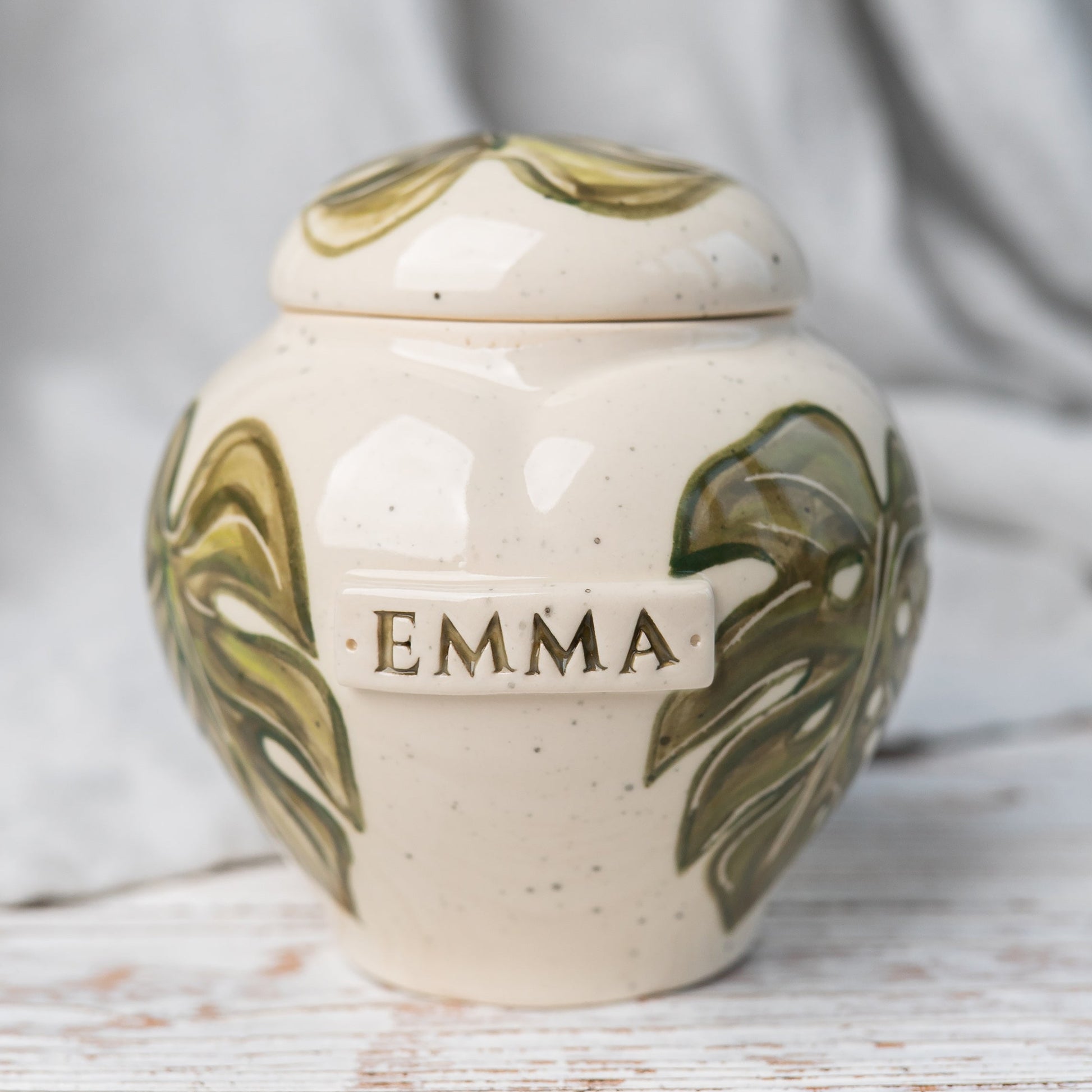 Front view of a white ceramic burial urn featuring a large, vibrant green monstera leaf