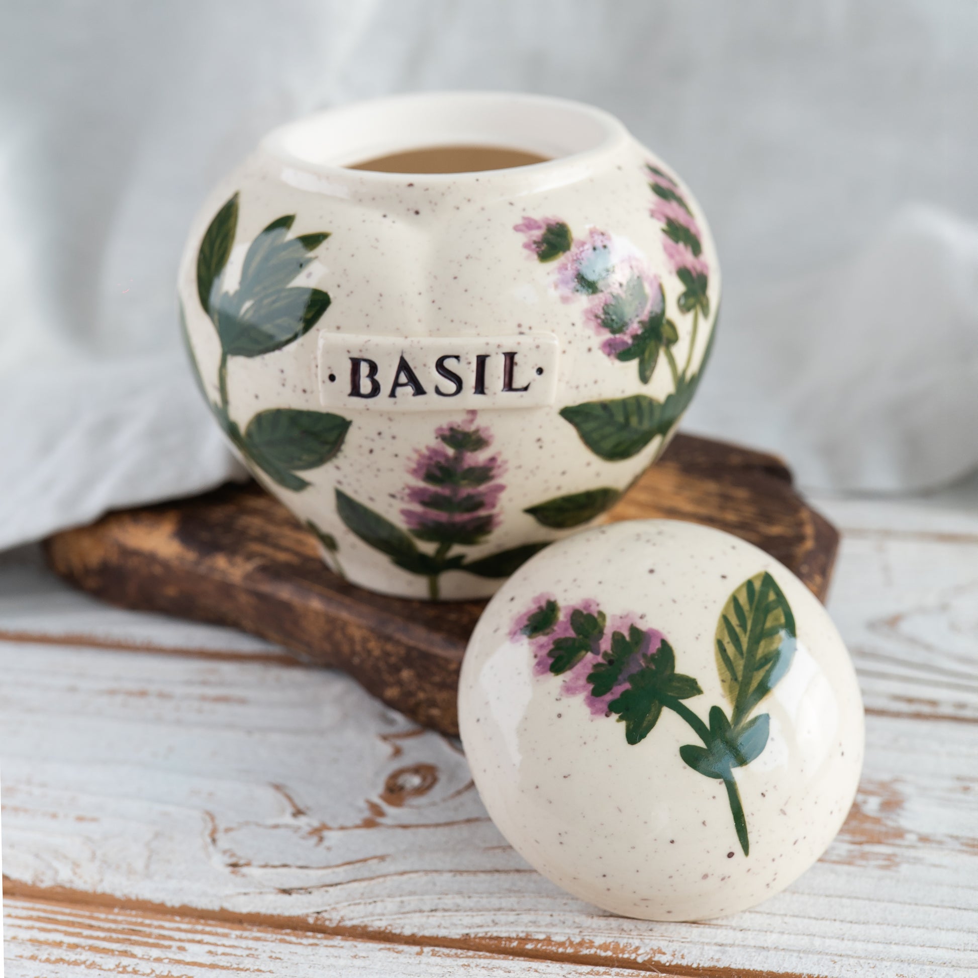 Open basil ceramic heart urn with lid resting beside it, showing the glazed interior and hand-painted green leaf details.