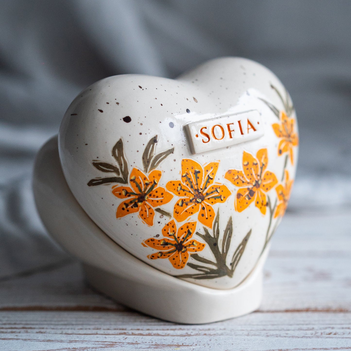 Side profile of the orange lily memorial urn on its stand, highlighting the smooth glaze and handmade quality.
